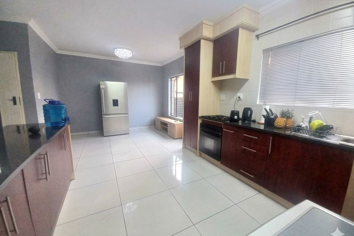 A functional kitchen featuring dark wood cabinetry, granite countertops, built-in oven, gas hob, and tiled flooring with ample space for a refrigerator.