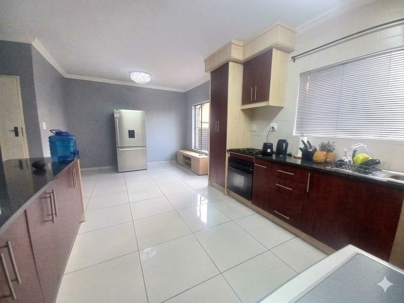 A functional kitchen featuring dark wood cabinetry, granite countertops, built-in oven, gas hob, and tiled flooring with ample space for a refrigerator.