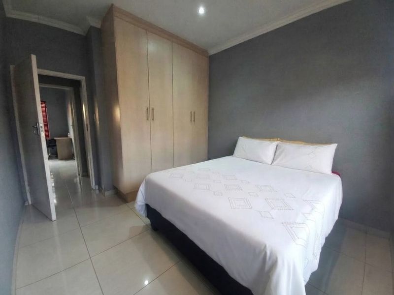 A well-maintained bedroom featuring neutral tiled flooring, built-in wooden cupboards, and recessed ceiling lighting, offering a clean and functional living space.