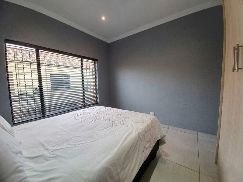 A bedroom featuring tiled flooring, built-in wardrobes, and venetian blinds, finished with neutral grey walls and coving.