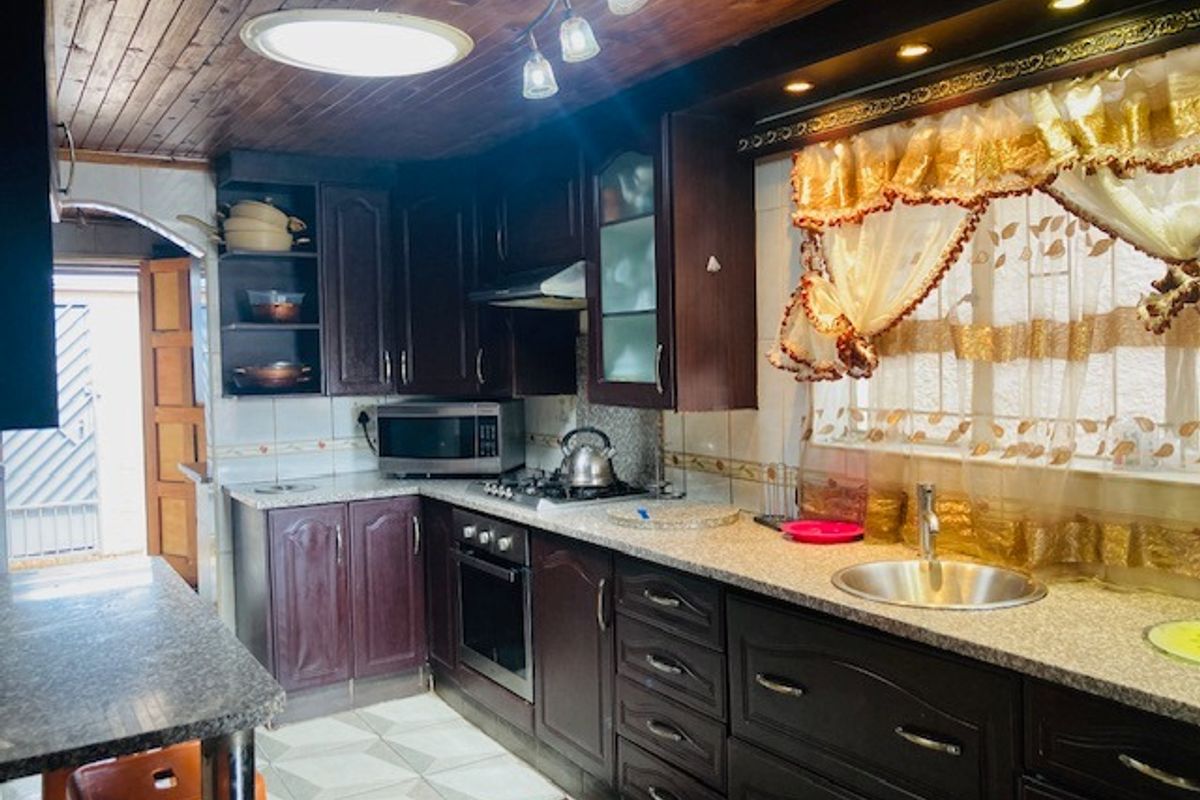 A functional kitchen featuring dark wood cabinetry, granite-style countertops, a built-in oven and hob, and a stainless steel sink.