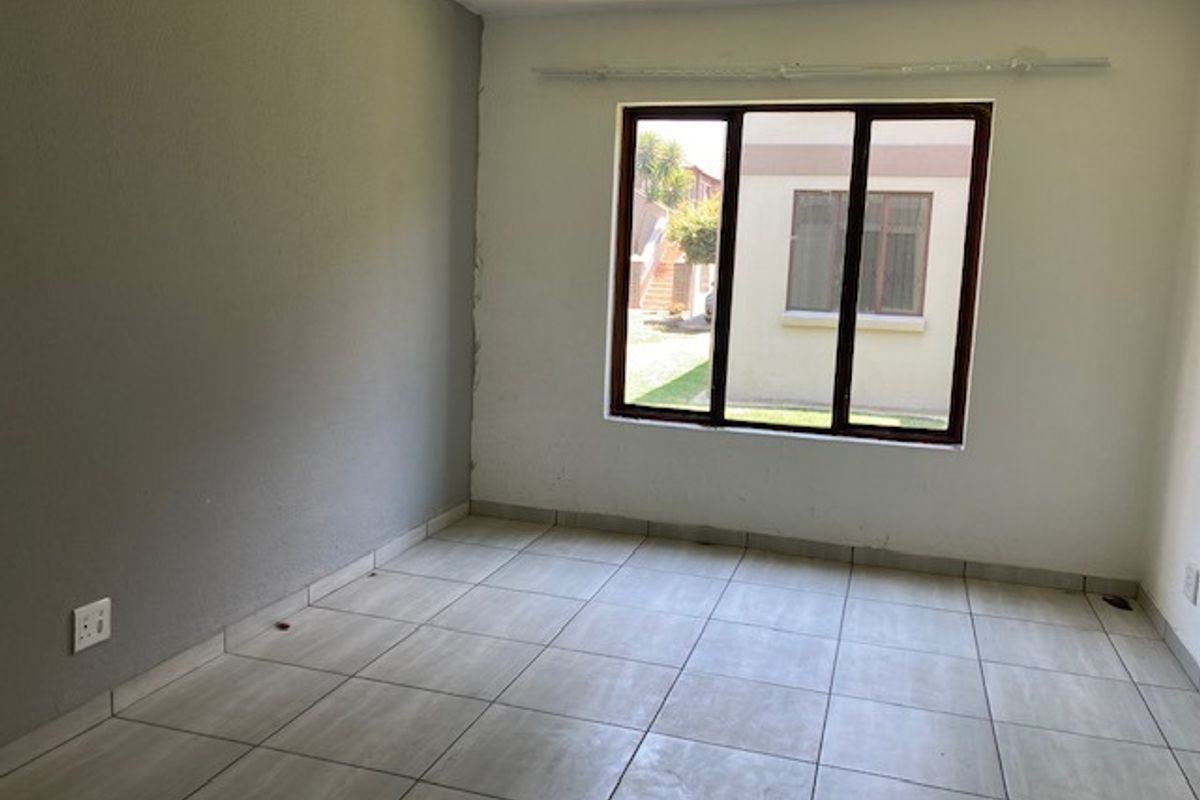 A vacant bedroom featuring neutral tiled flooring, a large window providing natural light, and a contrasting grey accent wall.