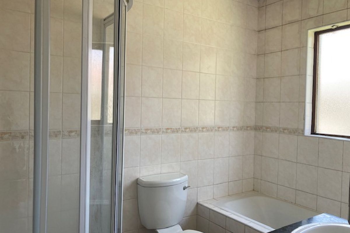 A dated bathroom featuring a corner shower enclosure, a built-in bathtub, a toilet, and a vanity sink with tiled walls.