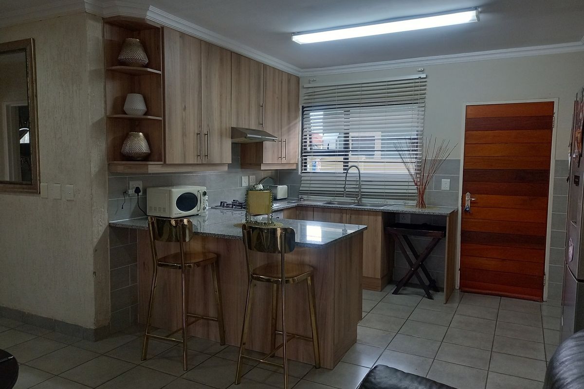 A functional kitchen featuring light wood cabinetry, granite countertops, a breakfast bar, stainless steel sink, and a built-in extractor fan.