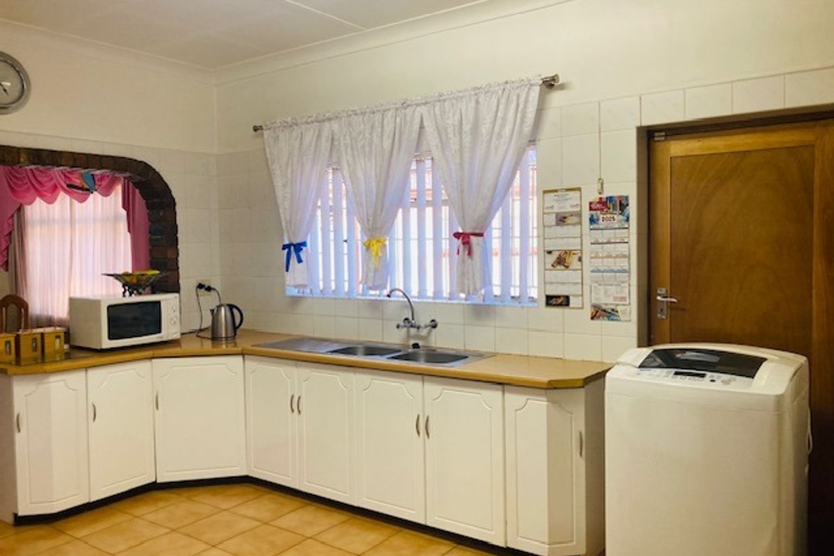 A functional kitchen featuring white cabinetry, double stainless steel sink, tiled splashbacks, and tiled flooring with a dedicated space for laundry appliances.