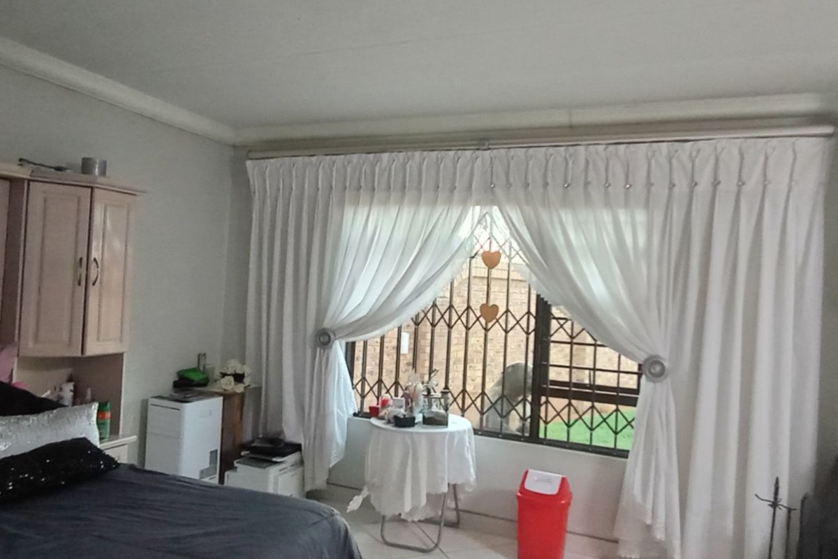 A bedroom featuring a built-in wardrobe unit and a freestanding fireplace, with large windows secured by metal security gates.