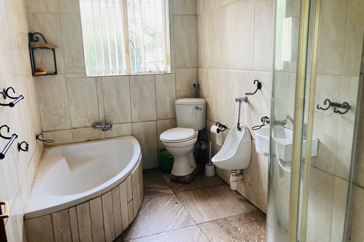 A functional bathroom featuring a corner bathtub, wall-mounted toilet, urinal, and a glass-enclosed shower stall with neutral wall and floor tiling.