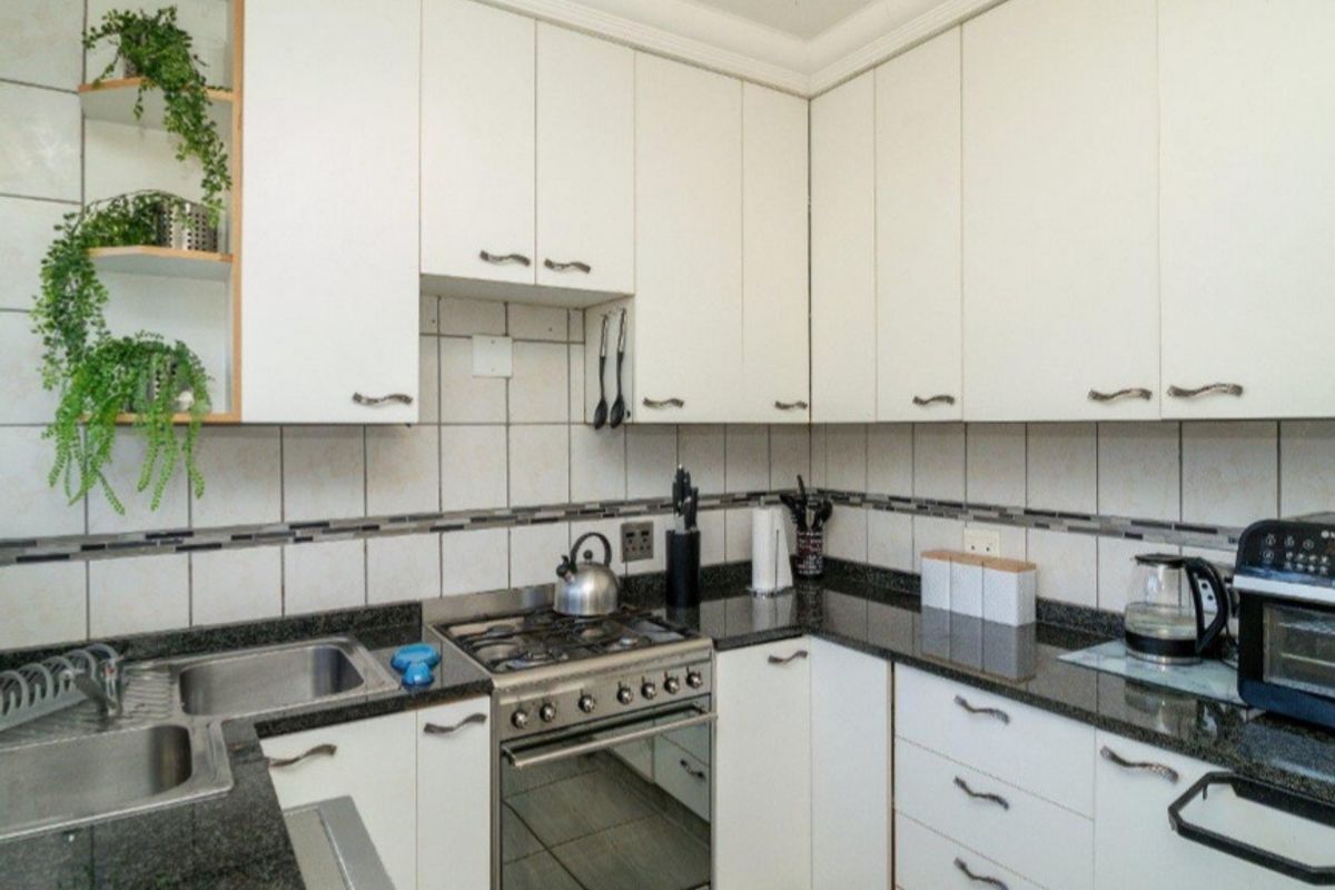 A functional kitchen featuring white cabinetry, dark granite countertops, a built-in gas stove with oven, and tiled splashbacks.