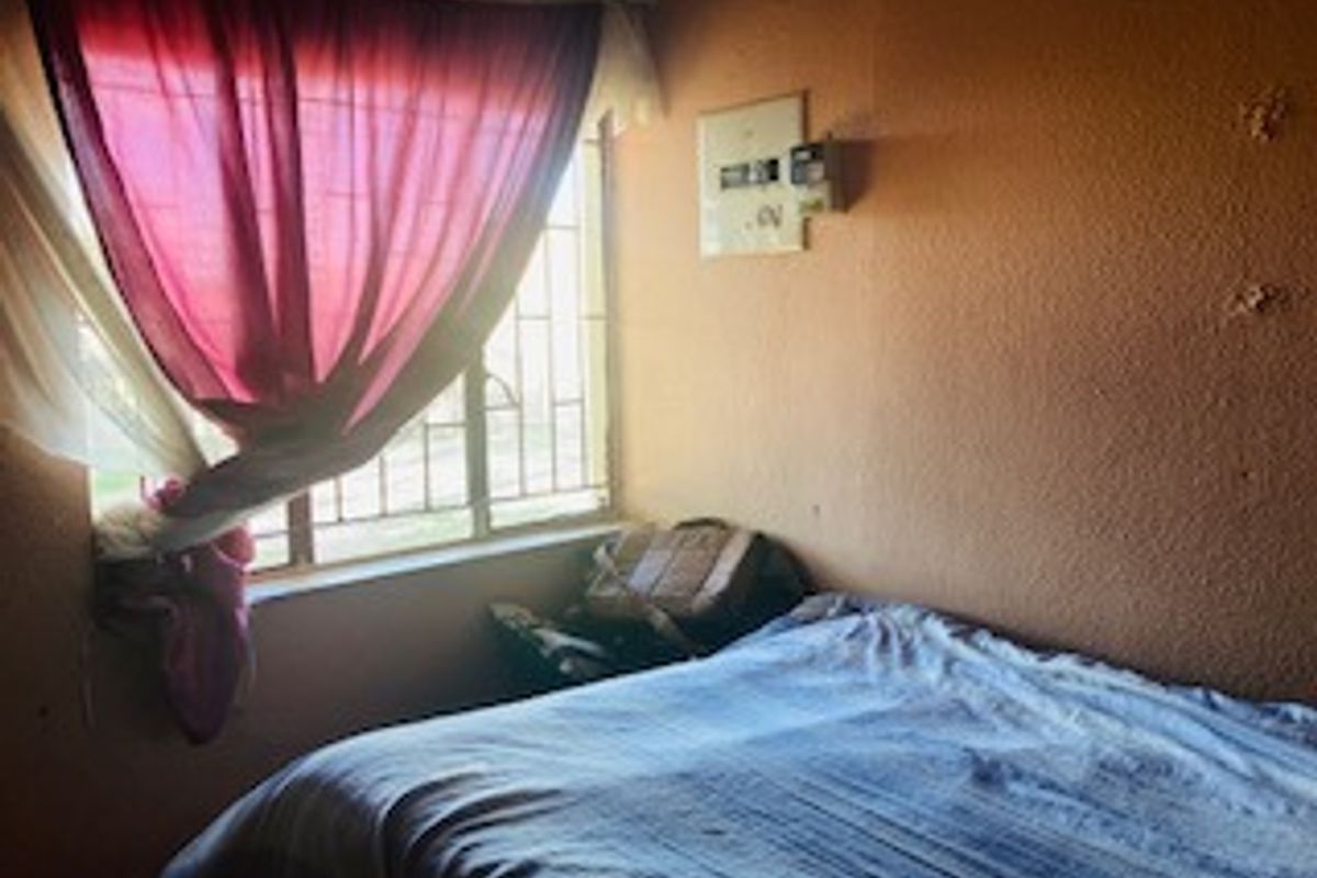 A bedroom featuring a window with security bars and an electrical distribution board mounted on the wall.