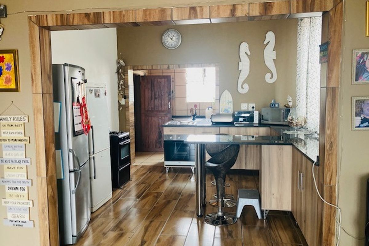 A functional kitchen featuring wood-look cabinetry, granite countertops, a breakfast bar, and tiled flooring, with an adjacent scullery area visible.
