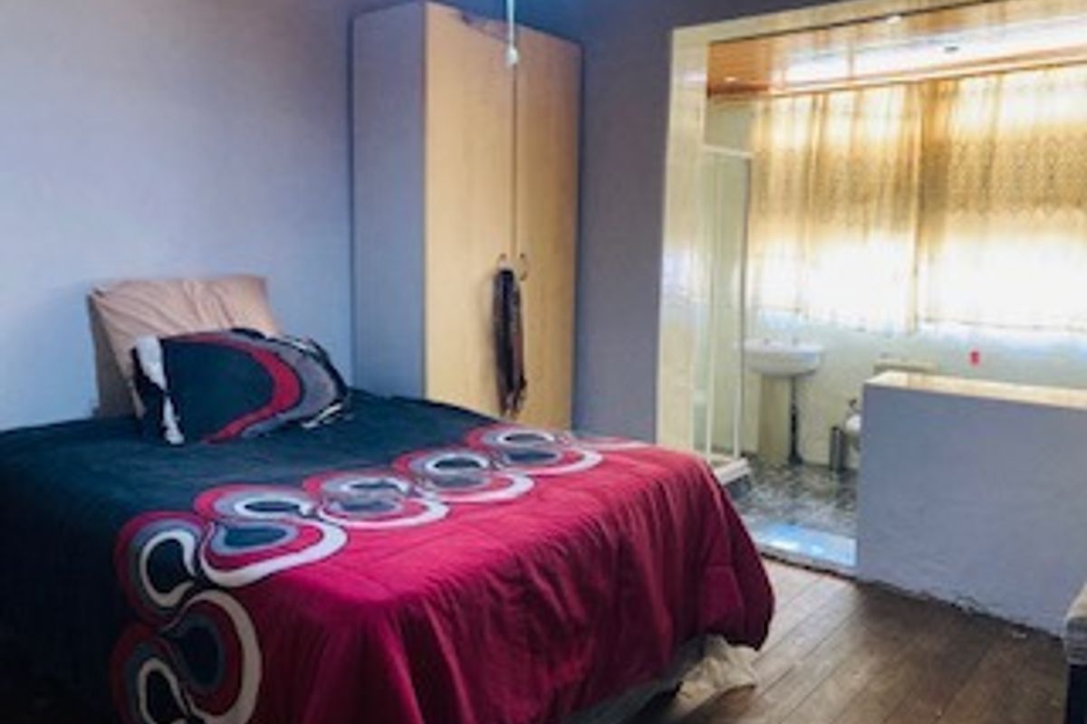 A bedroom featuring a built-in wardrobe and an open-plan en-suite bathroom with a pedestal sink and shower area.