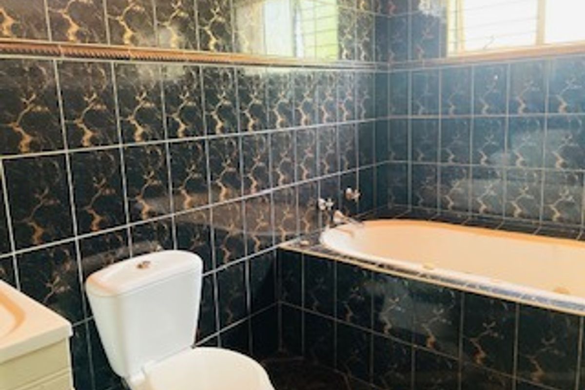 A dated bathroom featuring dark patterned wall tiles, a built-in bathtub, and a standard toilet suite.