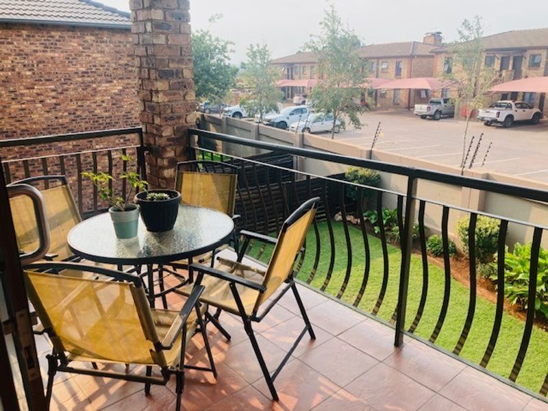 A private balcony featuring tiled flooring, a sturdy metal balustrade, and a brick pillar, overlooking the complex grounds and parking area.