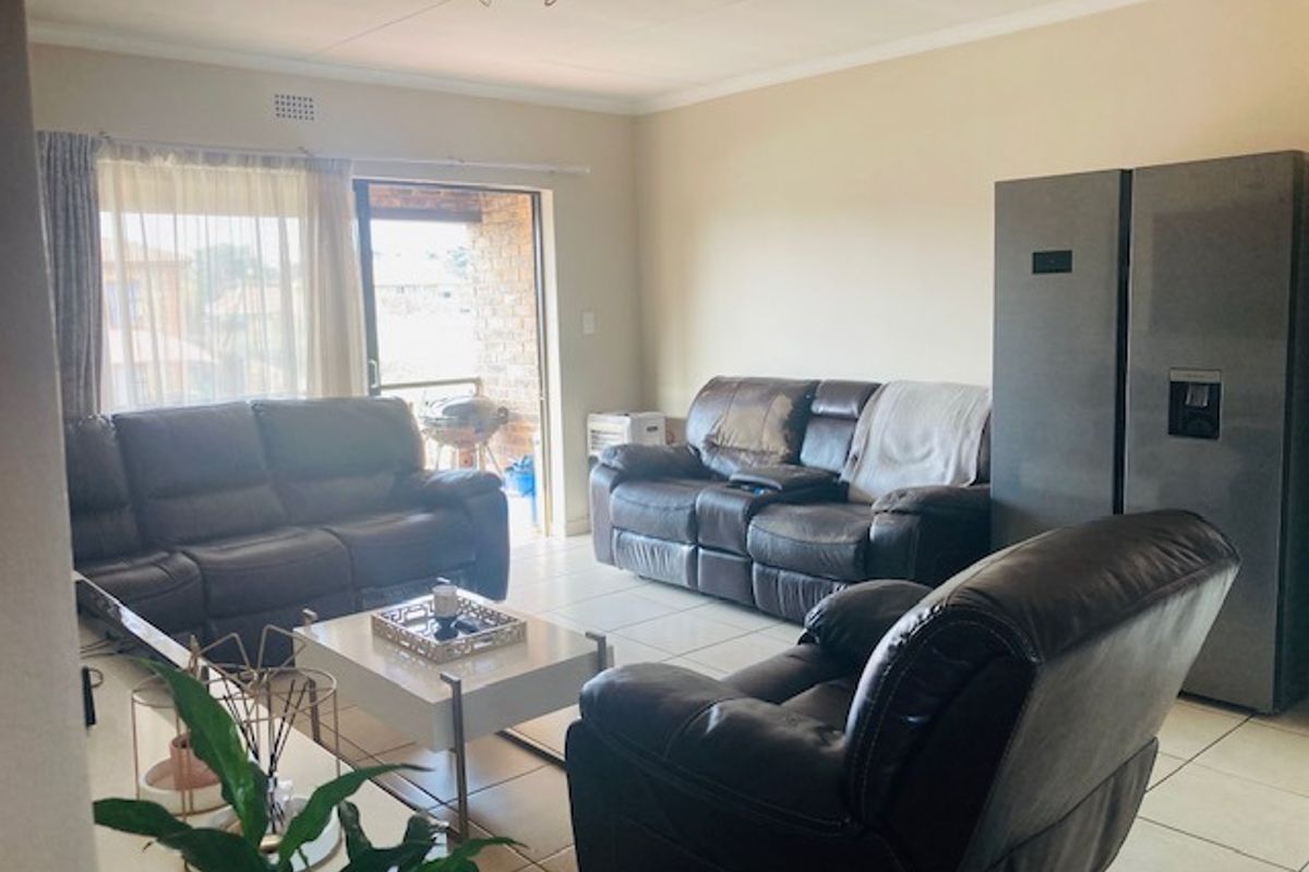 A spacious living room featuring neutral tiled flooring and a sliding glass door providing access to an outdoor balcony area.