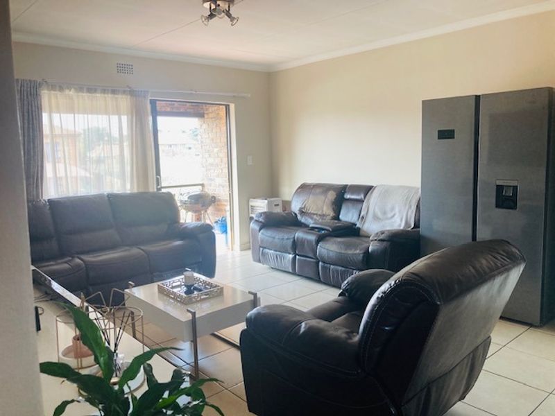 A spacious living room featuring neutral tiled flooring and a sliding glass door providing access to an outdoor balcony area.