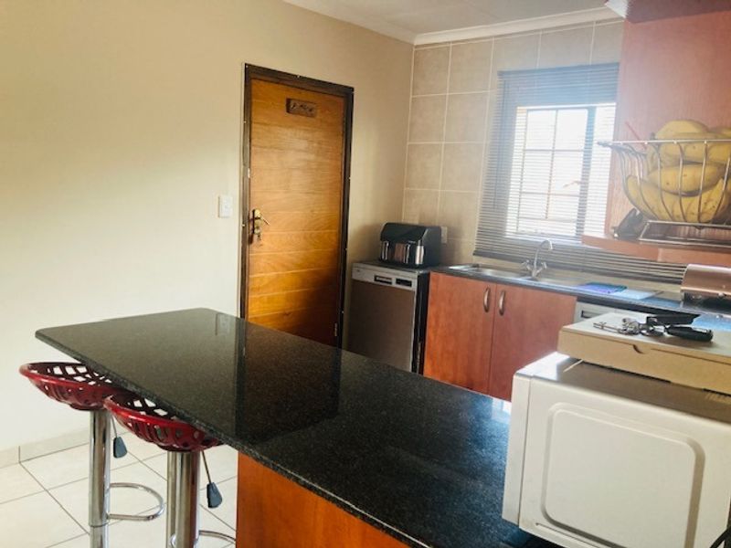 A functional kitchen featuring a granite breakfast bar, wooden cabinetry, tiled backsplash, and a window providing natural light.
