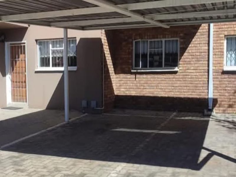 Covered carport area with paved flooring, brick exterior facade, and security features on windows and entrance.