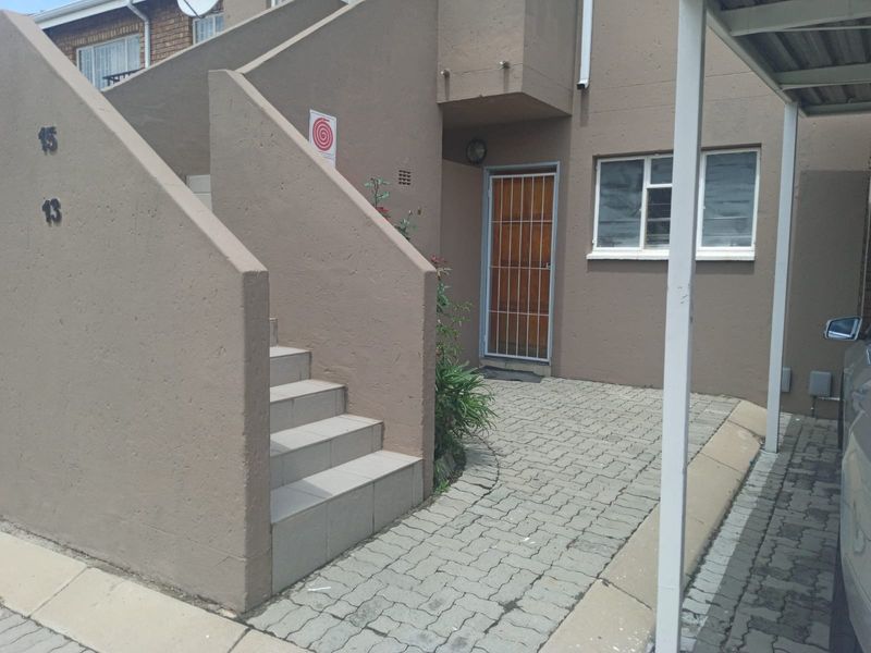 Exterior view of the apartment entrance featuring a paved driveway, carport, and external staircase leading to the upper level.