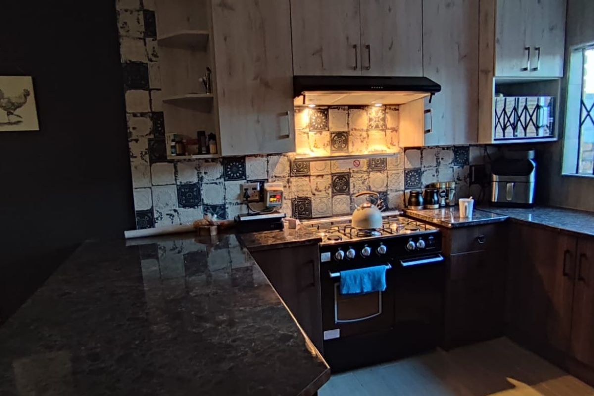 A functional kitchen featuring dark granite countertops, built-in cabinetry, a gas stove with an extractor fan, and a decorative tiled backsplash.
