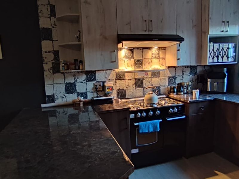 A functional kitchen featuring dark granite countertops, built-in cabinetry, a gas stove with an extractor fan, and a decorative tiled backsplash.