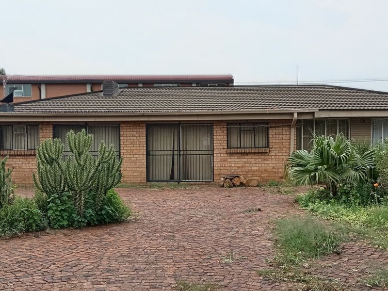 Rear view of a single-story brick house featuring a tiled roof, security gates, and a paved courtyard area with established garden beds.