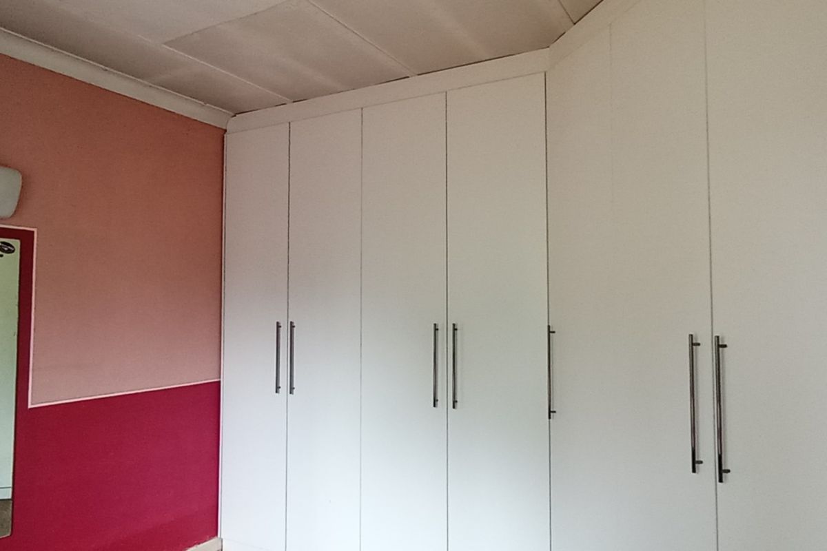 A bedroom featuring extensive white built-in cupboards and a wall-mounted light fixture, providing ample storage space.