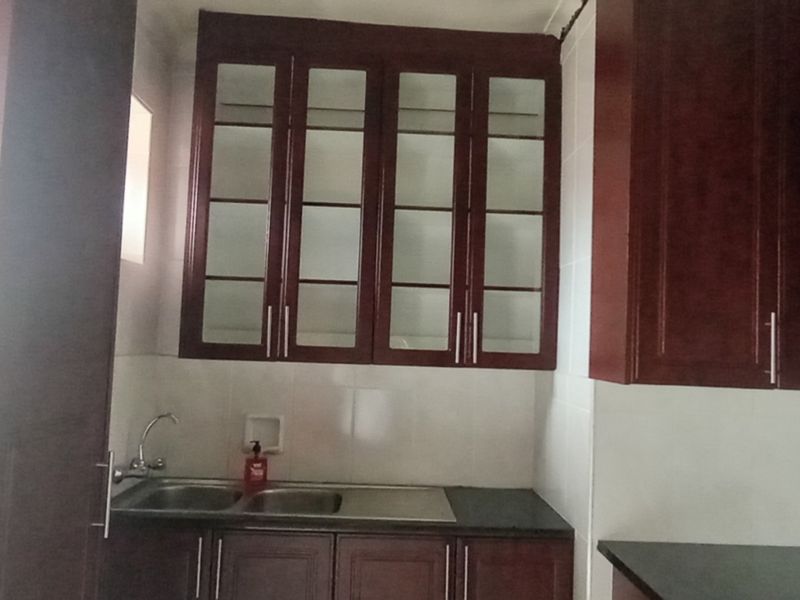 A functional kitchen area featuring dark wood cabinetry, glass-fronted upper storage, a stainless steel double sink, and tiled backsplash.