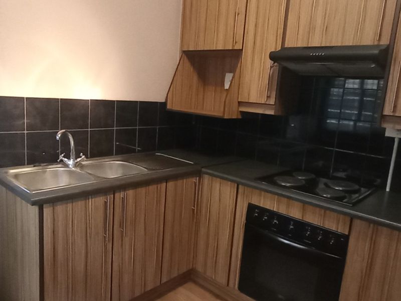 A functional kitchen featuring wood-look laminate cabinetry, a double bowl sink, black tiled splashback, and built-in electric cooking appliances.