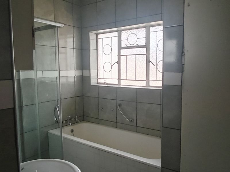 A functional bathroom featuring a bathtub, shower enclosure, and tiled walls, offering a blank canvas for modern renovation and aesthetic updates.