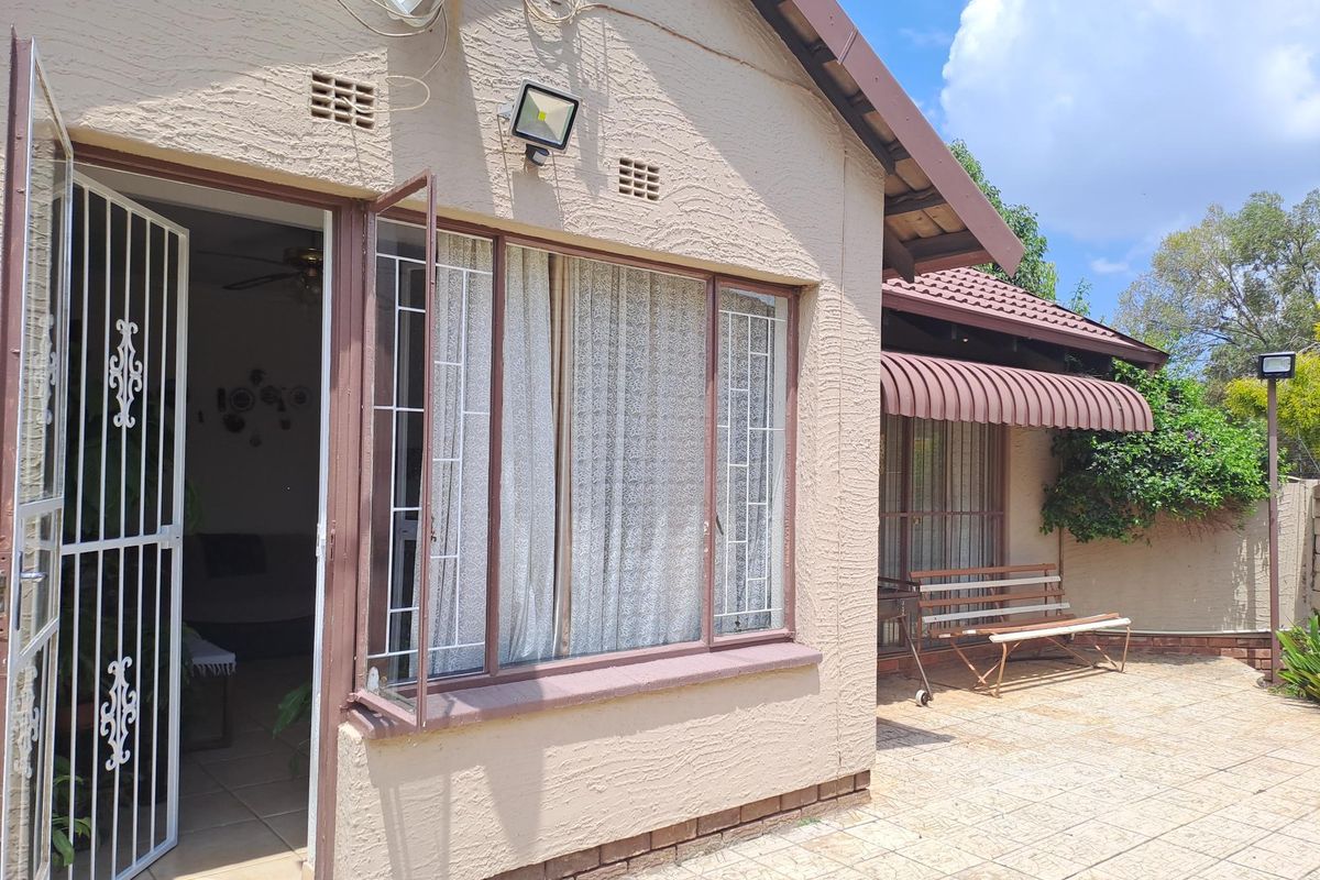Rear exterior view of the house featuring a tiled patio area, security gates, and metal window frames with an attached awning.