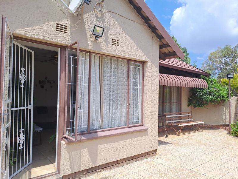 Rear exterior view of the house featuring a tiled patio area, security gates, and metal window frames with an attached awning.