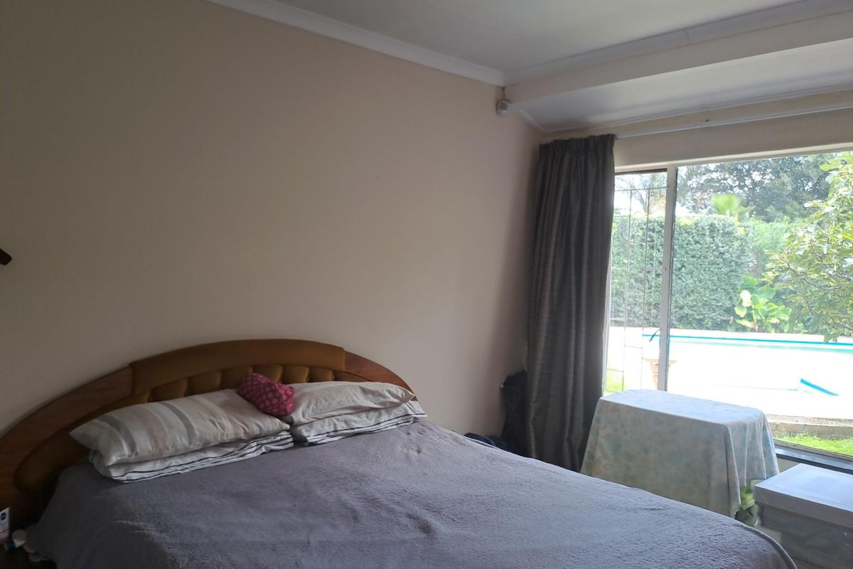 A bedroom featuring a sliding glass door with security gate, providing direct access to the outdoor pool area.