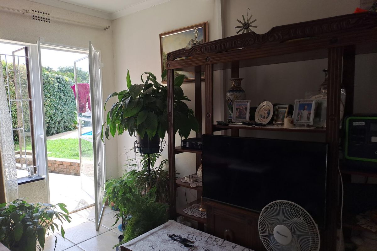 A living room area featuring tiled flooring and a glass door providing direct access to the outdoor garden and pool area.