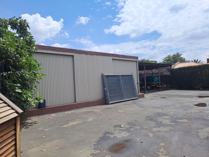 Rear exterior view showing a corrugated metal structure, paved driveway area, and an attached carport.