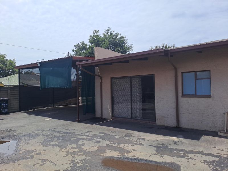 Rear exterior view of the property featuring a sliding glass door, a covered carport area, and an asphalt driveway with visible wear.