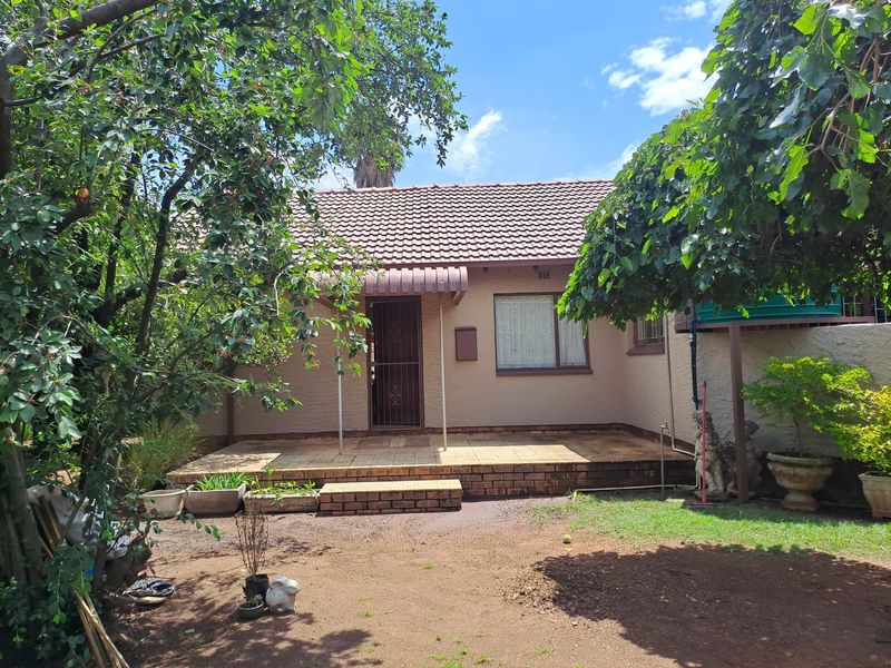 A rear view of the house featuring a tiled patio area, brick steps, and a tiled roof, surrounded by a garden with mature trees.