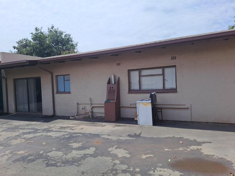 Rear exterior view of the property featuring a paved driveway, sliding door access, and standard window finishes.