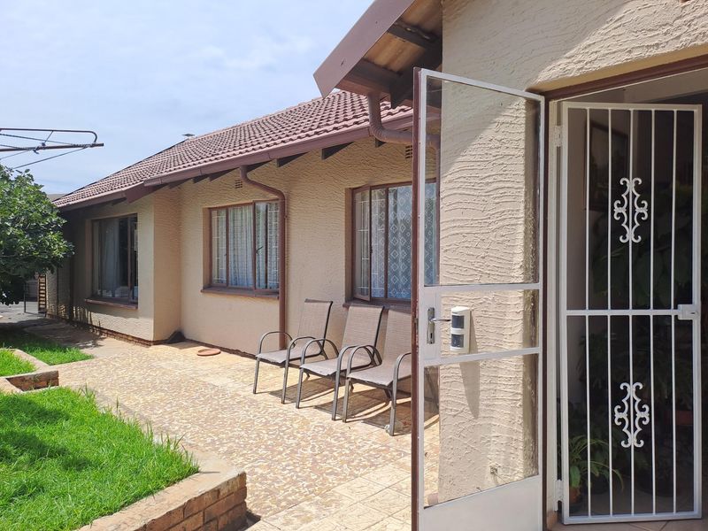 A rear exterior view of the house featuring a paved patio area, brick retaining wall, and secure entrance gate.