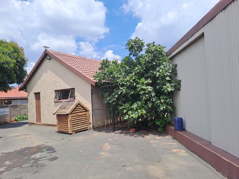 Rear exterior view of the property featuring a tiled roof, textured plaster walls, and adjacent metal-clad structure with paved driveway access.
