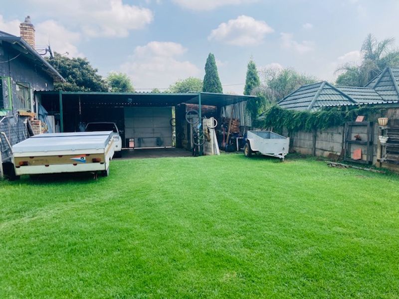 Rear garden area featuring a large lawn, a metal carport structure, and perimeter boundary walls.