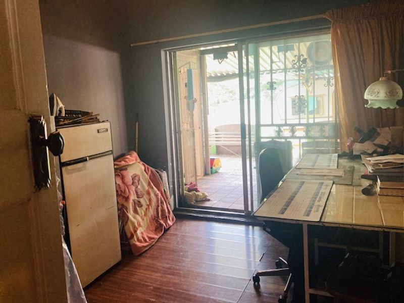 A small office or study area featuring laminate flooring and a sliding glass door with security gate leading to an outdoor patio.