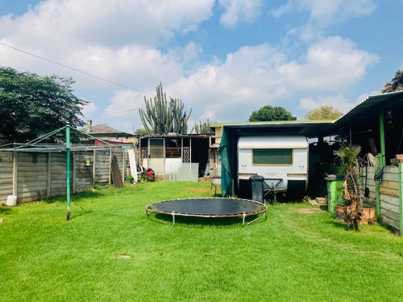A spacious rear garden featuring a lawn, a precast concrete boundary wall, and a covered carport area.