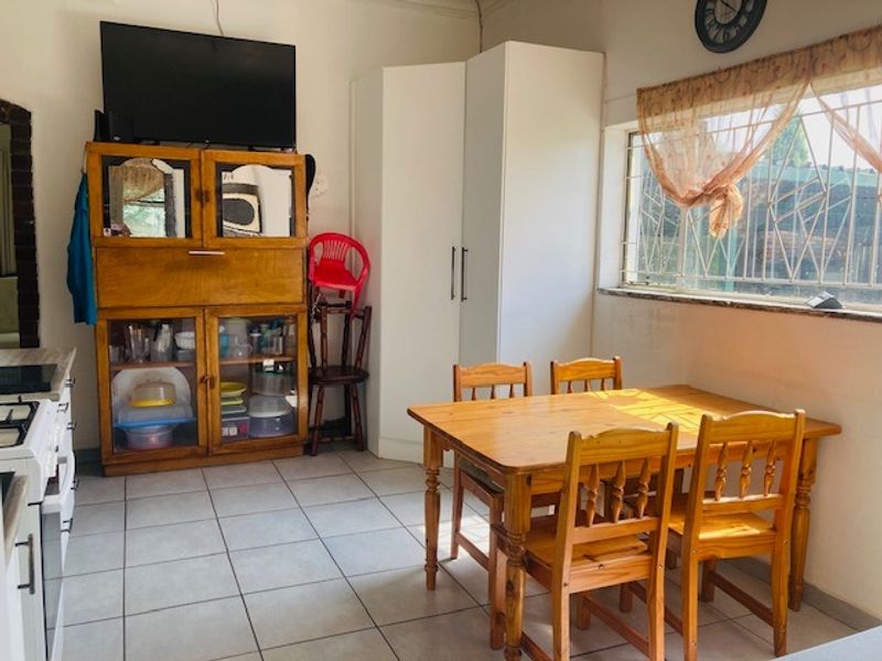 Open-plan living and dining area featuring tiled flooring, a built-in cupboard, and a window with security bars.