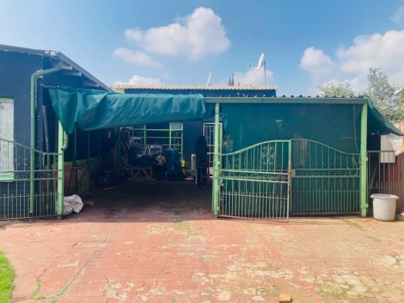 Rear exterior area featuring a paved driveway, metal security gate, and a shade cloth canopy structure attached to the building.