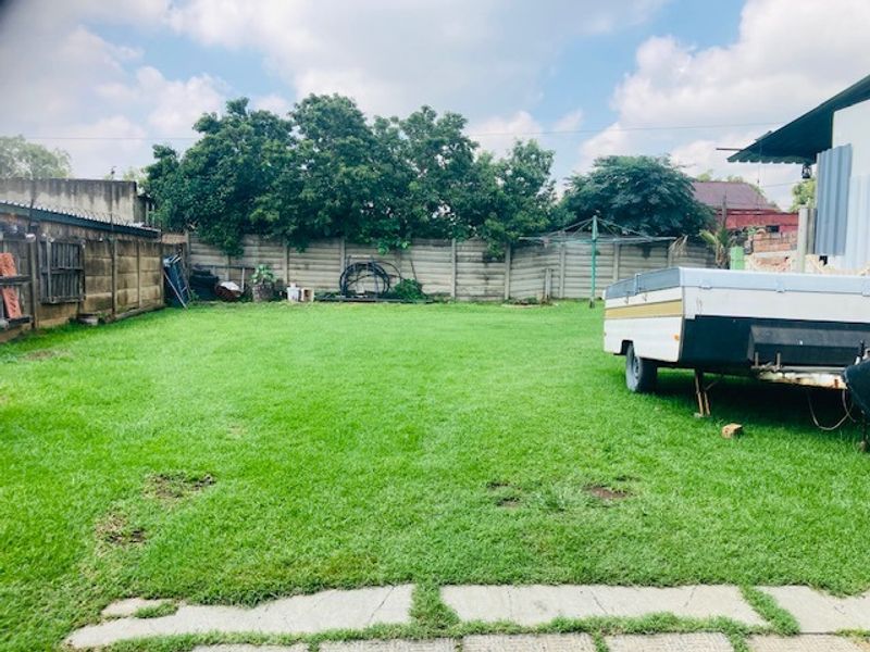 A spacious, level backyard featuring a well-maintained lawn, enclosed by precast concrete boundary walls and including a paved walkway.