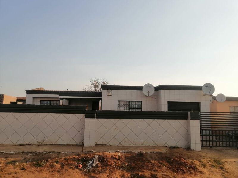 Front exterior view of a single-story house featuring a tiled facade, perimeter wall, security gate, and integrated garage.