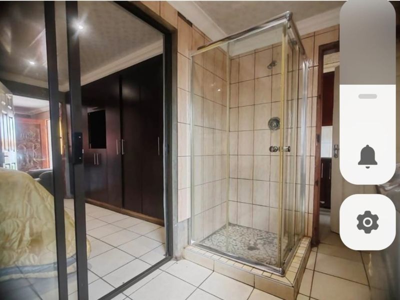 Bedroom featuring an en-suite shower enclosure, tiled flooring, and built-in cupboards, showing signs of dated finishes.