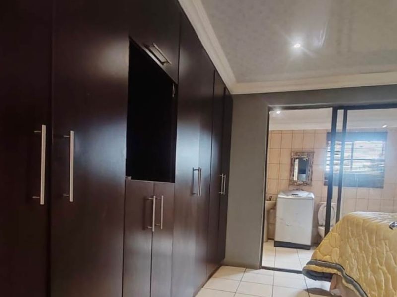 Bedroom featuring dark wood built-in cupboards, tiled flooring, and direct access to an en-suite bathroom with tiled walls.