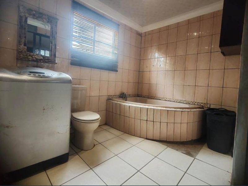 A dated bathroom featuring a built-in bathtub, ceramic wall and floor tiles, and a standard toilet, requiring cosmetic updates to modernize the space.