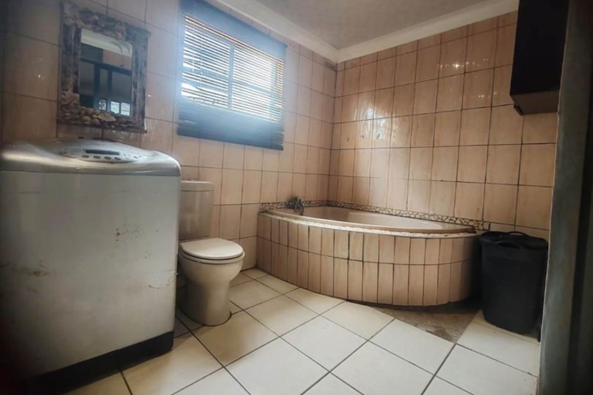 A dated bathroom featuring a built-in bathtub, ceramic wall and floor tiles, and a standard toilet, requiring cosmetic updates to modernize the space.